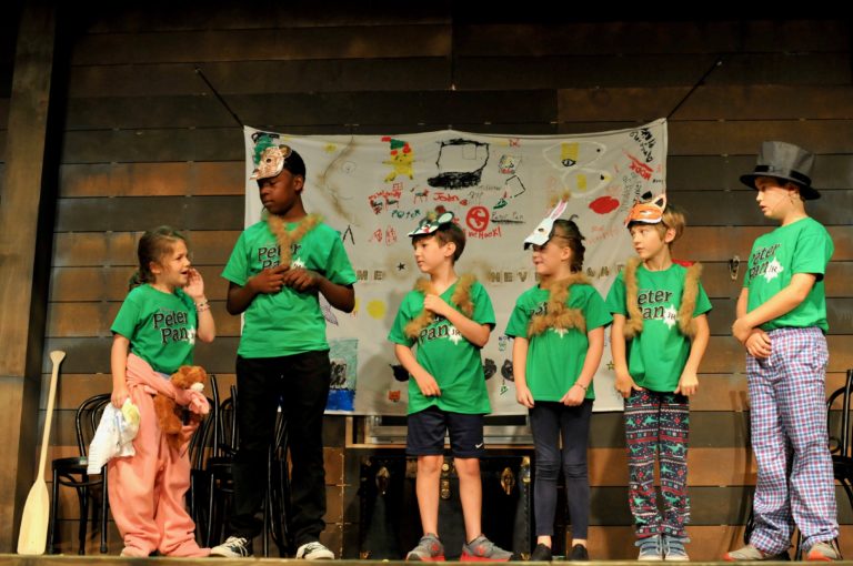 Six children stand in a line while wearing green shirts and animal masks