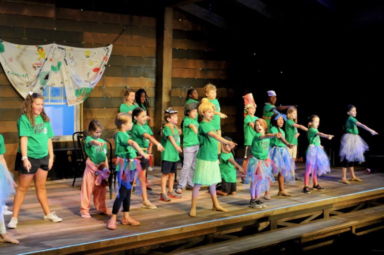 The whole cast is pointing downstage while wearing green shirts