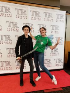 Two young women pose in front of the photo booth. It has a white background featuring the TR logo and a red carpet
