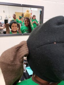 A boy wearing dog ears smiles at his reflection in dressing room mirror.