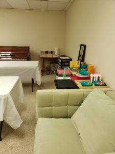 A clean craft room with two empty white tables. Art supplies are bunched together against one wall