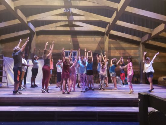 The cast of Peter Pan Jr. onstage, standing in a circle and raising their arms high