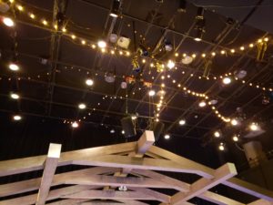 Twinkly light bulbs hang from the ceiling above wooden rafters