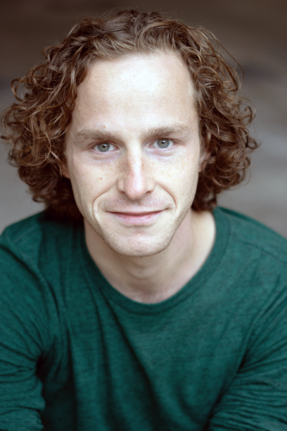 A man with curly red hair and light skin wearing a dark green shirt