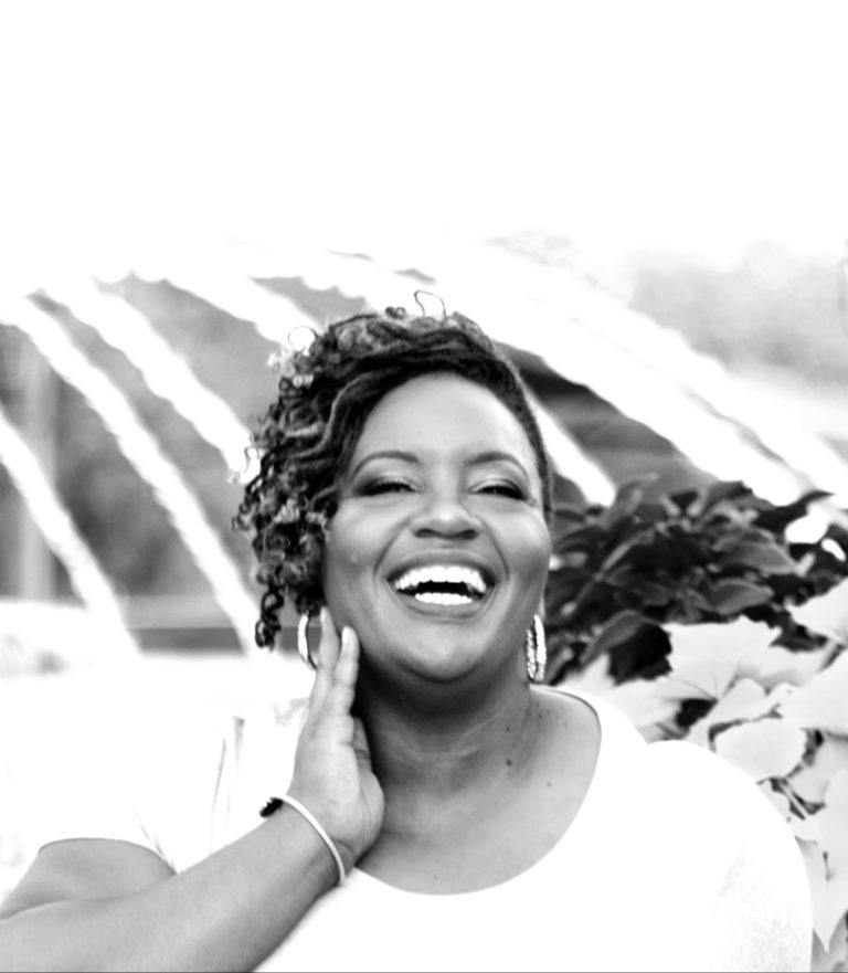 A young woman with dark skin skin wearing a white shirt and laughing